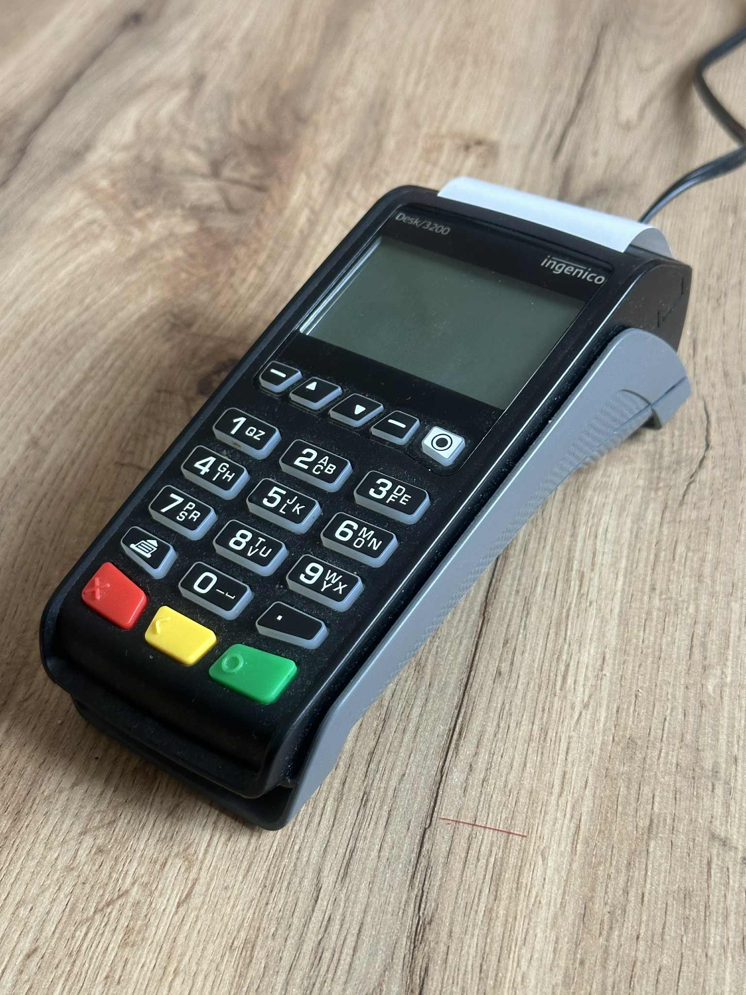 An Ingenico payment terminal with keypad and receipt roll on a plain surface